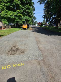 Compact excavation equipment on a prepared gravel work area beside a road