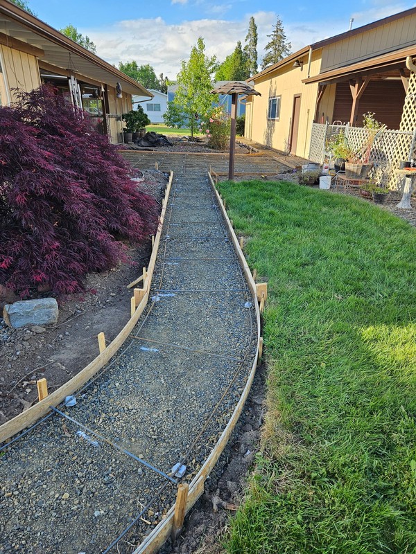 Curved concrete walkway and patio area during base preparation and reinforcement for a residential backyard flatwork project.